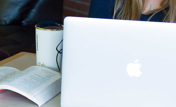 An open book  next to an open laptop and a travel coffee mug]