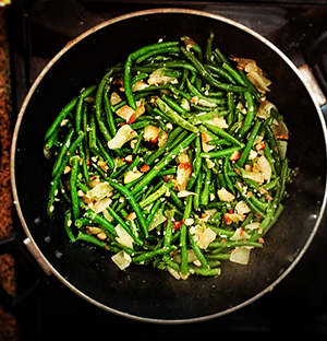 Green beans and almonds simmer in a wok on the stove.