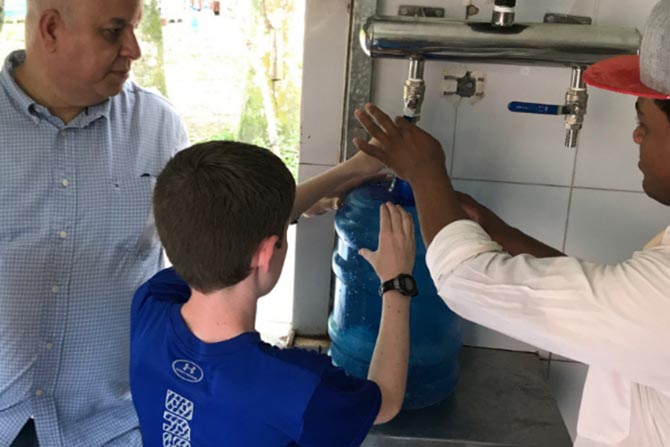 Two men from the Dominican Republic show a young boy how to filter clean water.