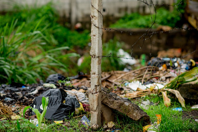 A barbwire fence next to a trash-contaminated water source