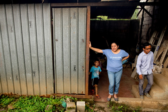 A Guatemalan woman wearing a 1040.com shirt stands next to a building