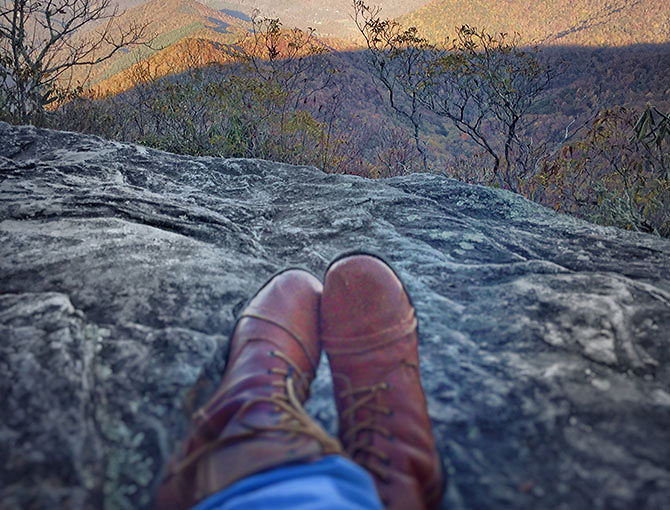 A hiker hangs her feet over the side of a rock overlooking the Blue Ridge mountains.