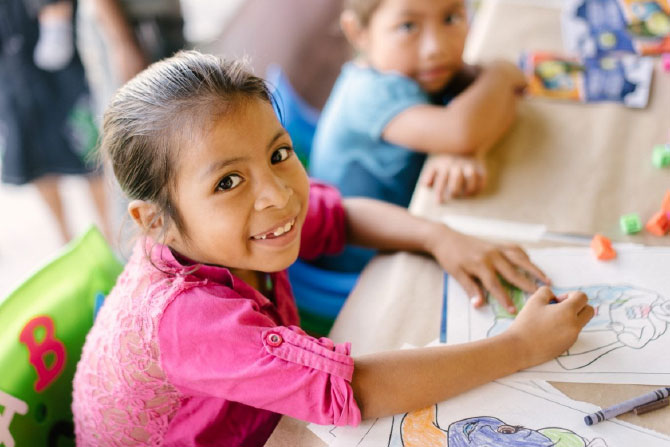 Mema grins over her crayons as she follows her dream to read and write.