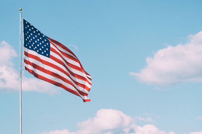 A United States flag waves against a blue sky.