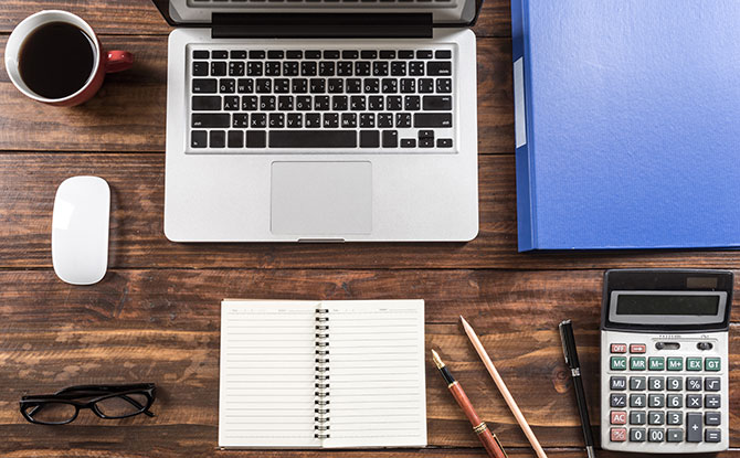 A laptop with notebooks, folders, pencils and a calculator on a wooden table