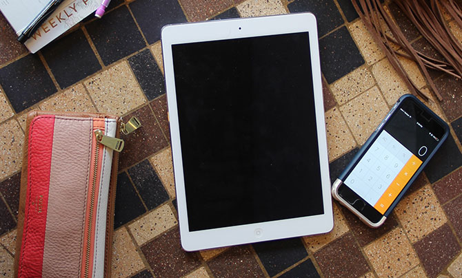 A wallet, iPad, and phone with the calculator app activated on a tile table