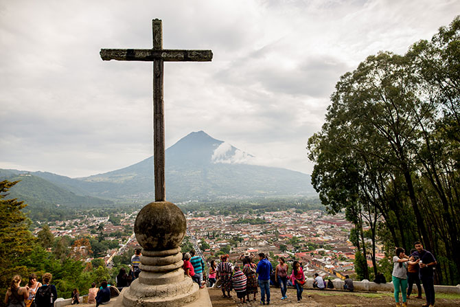 A scenic overlook in Antigua, Guatemala with a view of the city, a giant cross and a volcano on the horizon
