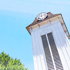 A whitewashed clock tower against a blue sky.]