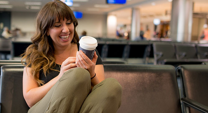 A woman smiles at her coffee cup while sitting in an airport.