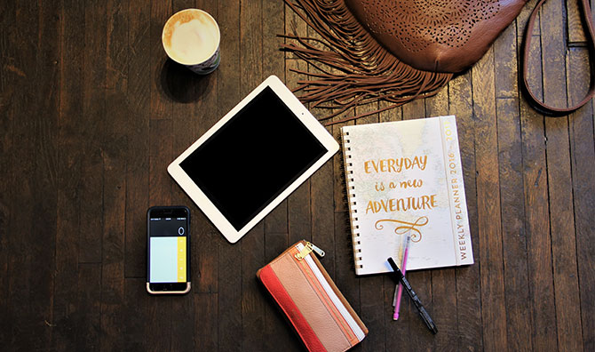 A phone, tablet, and planner on a hardwood background.