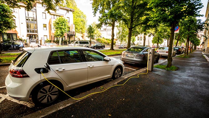 Plug-in electric and hybrid cars being recharged in a green neighborhood.