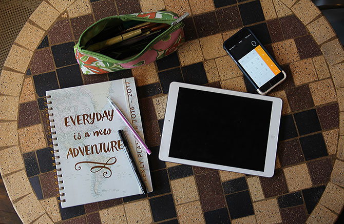 A tablet, phone, and planner  on a coffee shop table.]