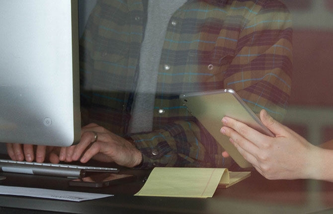  A woman using a tablet while a man types on a computer.]