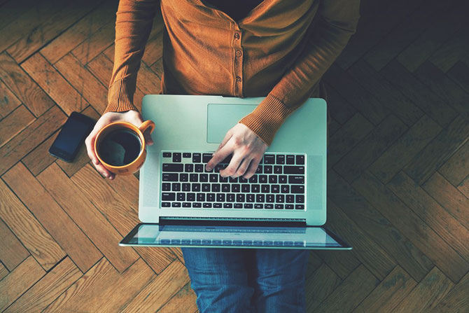 A person working on a  laptop, coffee in hand