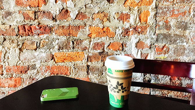 A phone and a coffee on a table next to a brick wall