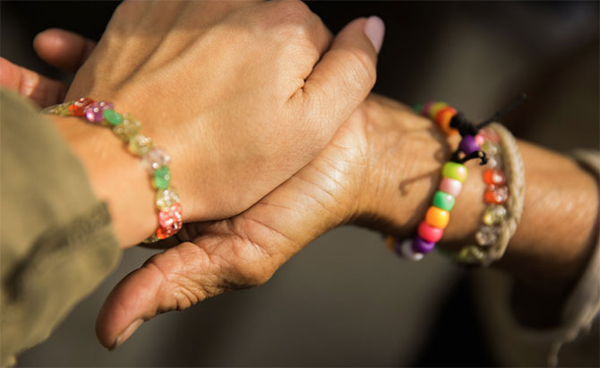 Two women holding hands, wearing handmade friendship bracelets.