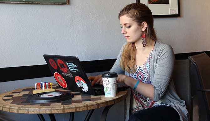 A girl using a stickered laptop in a café.