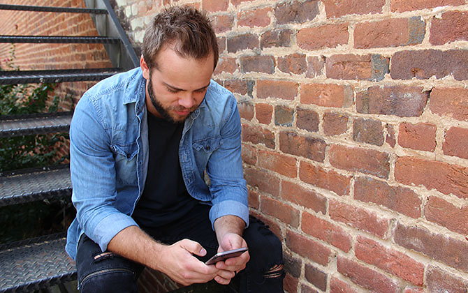 Man sits on steps outside brick building and manages his account on mobile.