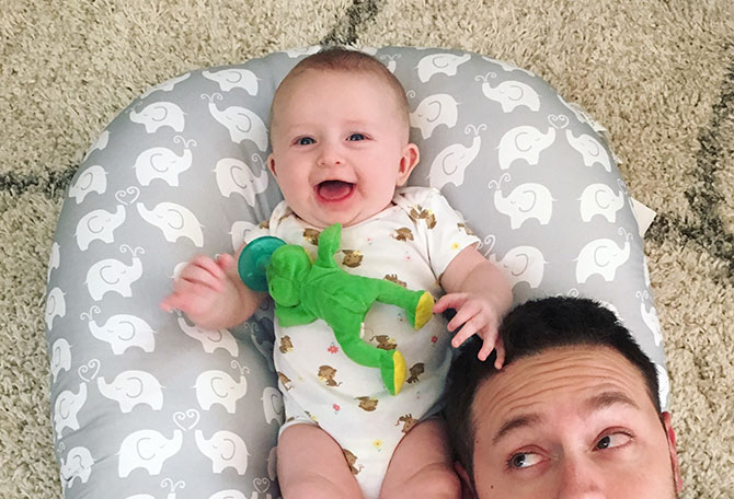 A baby girl laughs on the floor with her dad.