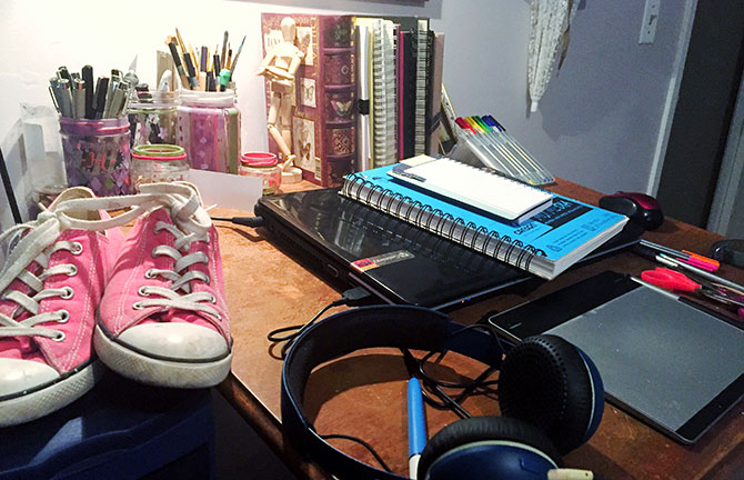 An artist’s desk, covered with pens and notebooks, sneakers and headphones