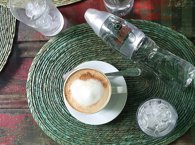 A place is set with coffee, bottled water, and ice on a red, wooden table.