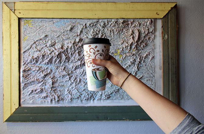 A woman holds up a cup of coffee in front of a topographical map.