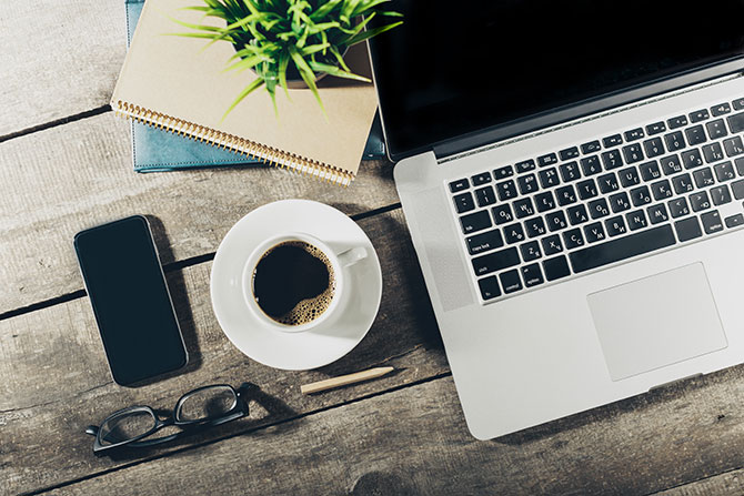 A laptop  on a desk with coffee, notebooks, and a smartphone]