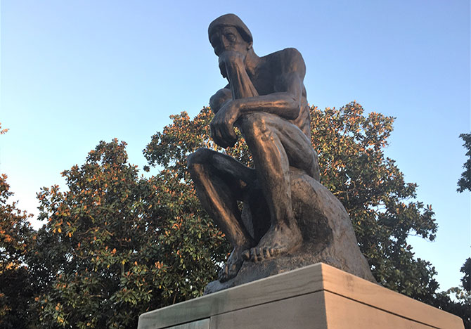 A replica of The Thinker against a blue sky