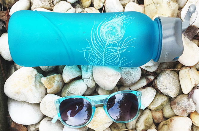 A blue water bottle and matching sunglasses on pebbles