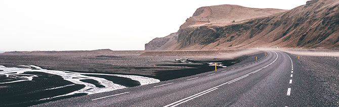 A winding road hugs Icelandic cliffs next to the sea.