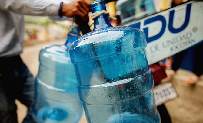 Five-gallon jugs tied to the back of a motorbike, ready for use]