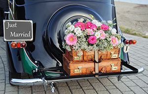Vintage car with  suitcases, a  bouquet of roses, and a “Just Married” sign
