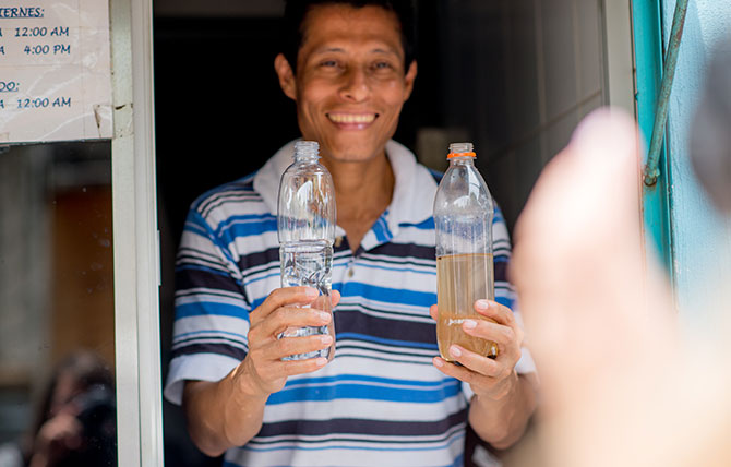 A Guatemalan man holds up a bottle of river water and a bottle of clean water to compare.