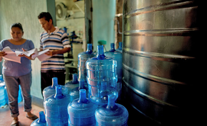 Two members of the Portales church review clean water information next to a stack of jugs.